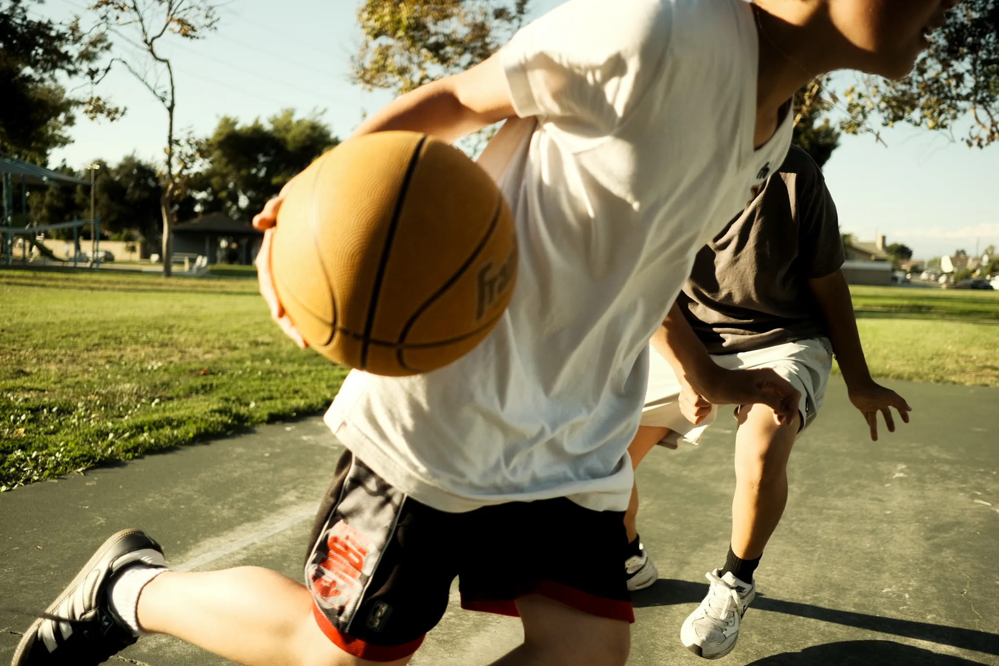 Pickup basketball game on an outdoor court, ball in hand mid-drive
