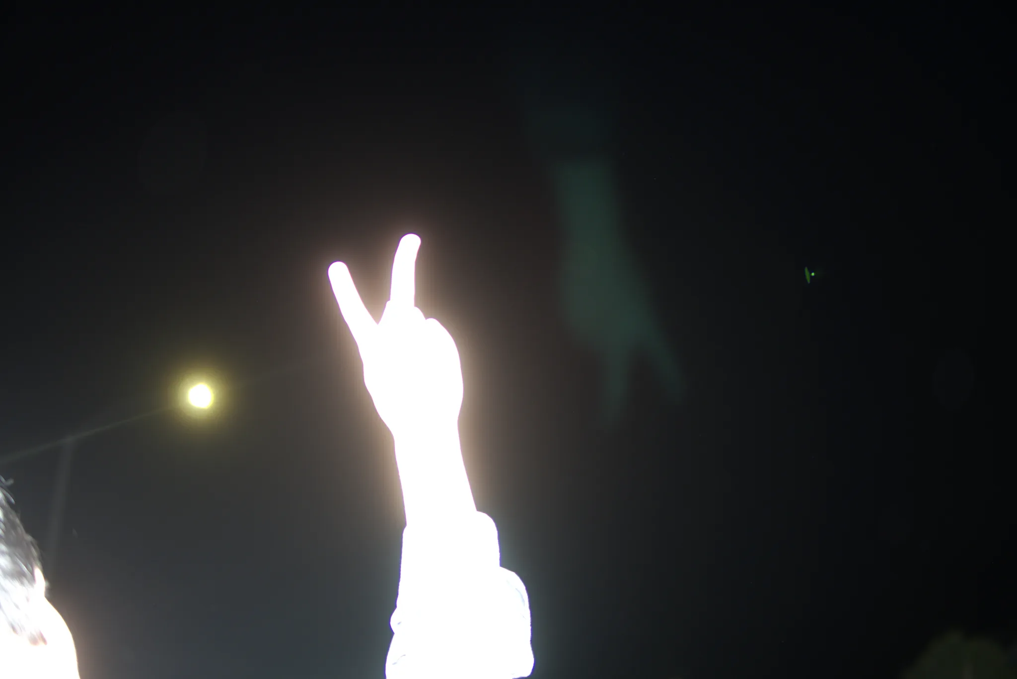 Overexposed hand flashing a peace sign against a dark night sky