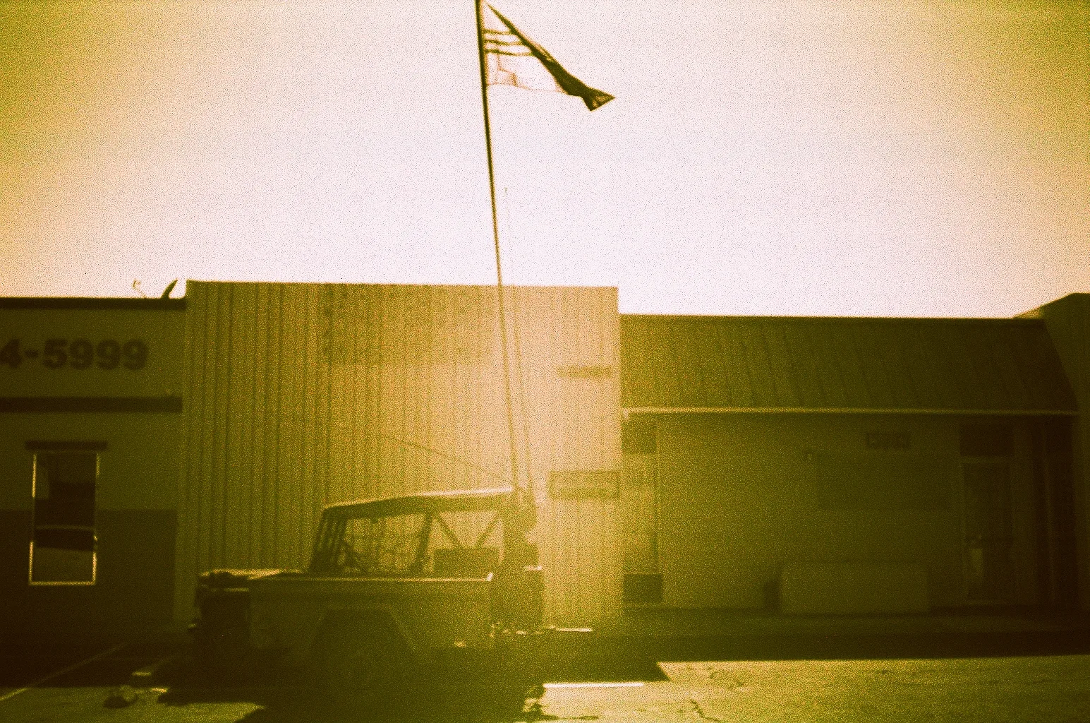 Old pickup truck parked beneath a flagpole, washed in warm expired-film tones