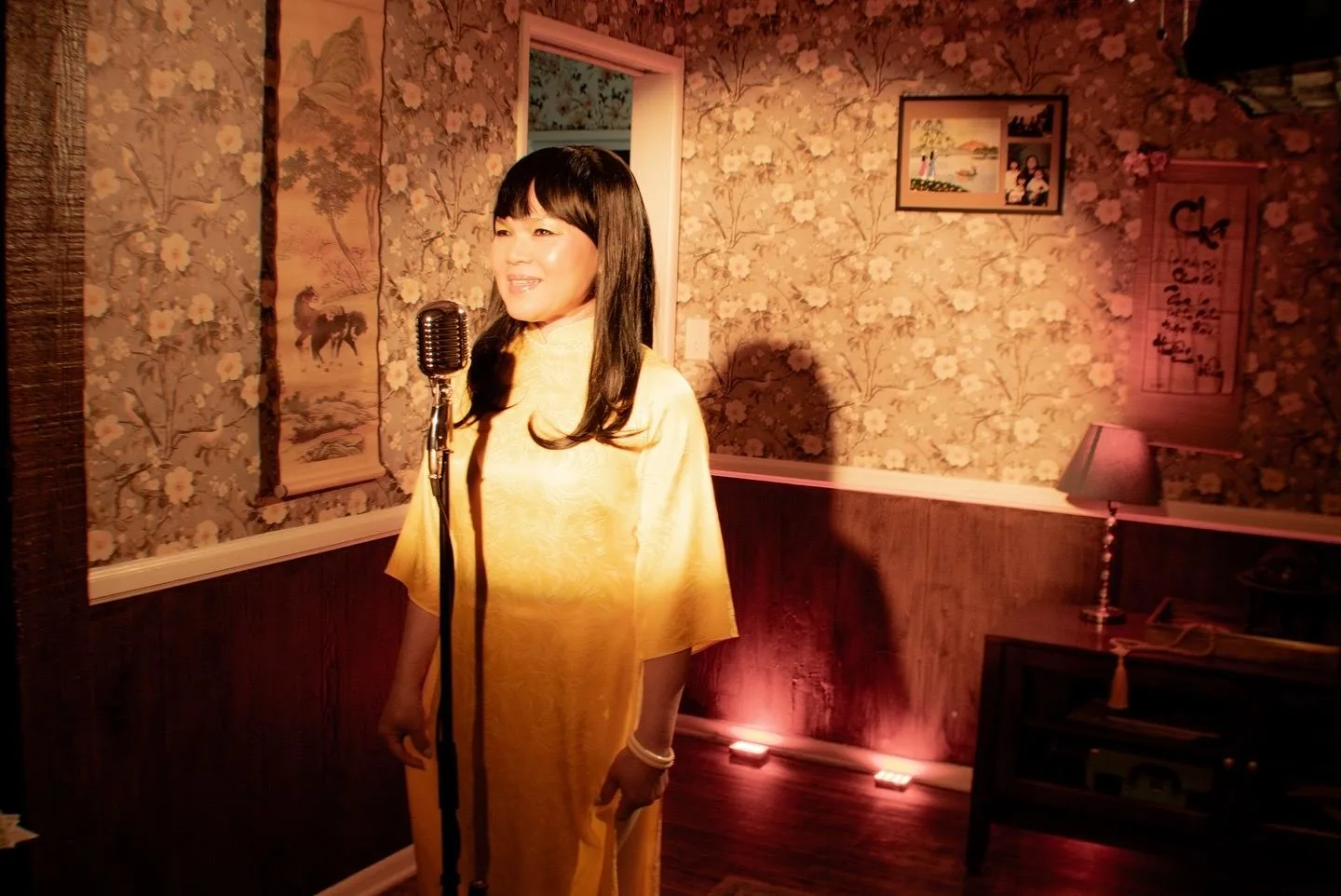Singer in a yellow áo dài at a vintage microphone in a warm wallpapered room