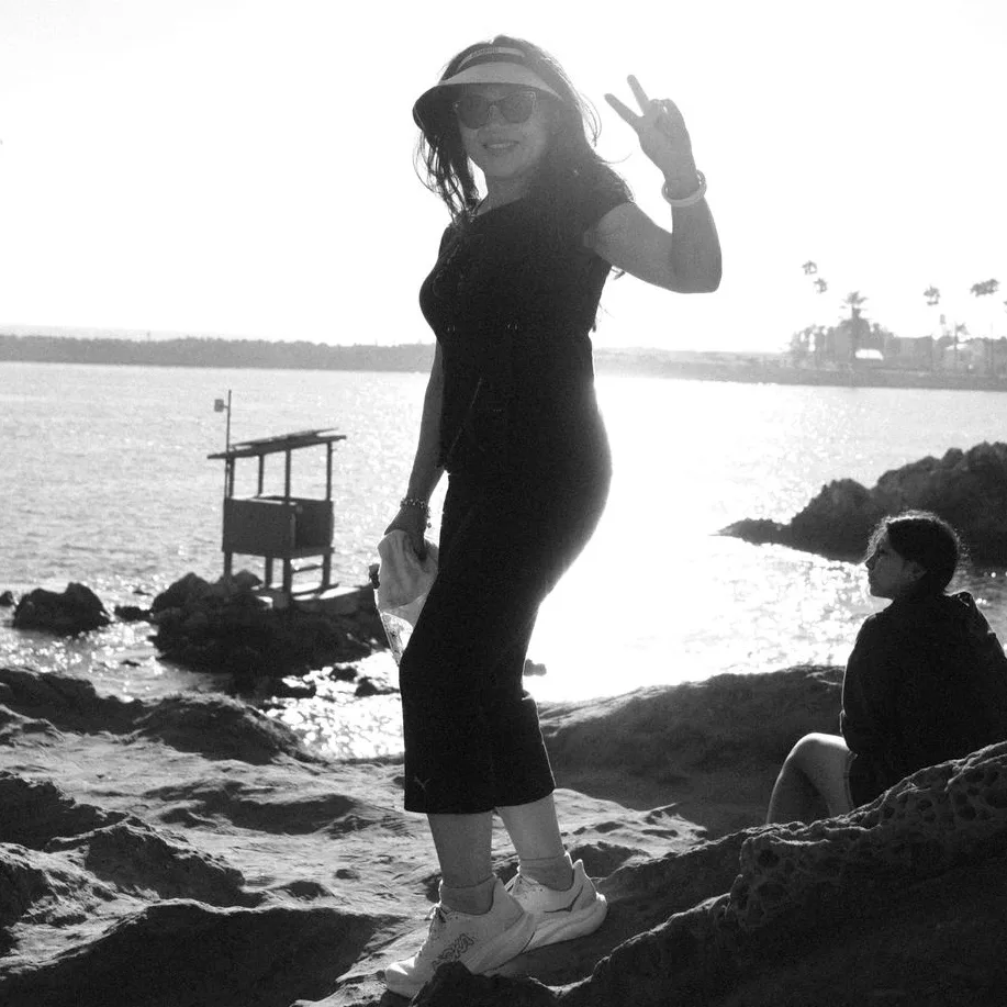 Black-and-white beach scene of a woman in a visor flashing a peace sign on the rocks