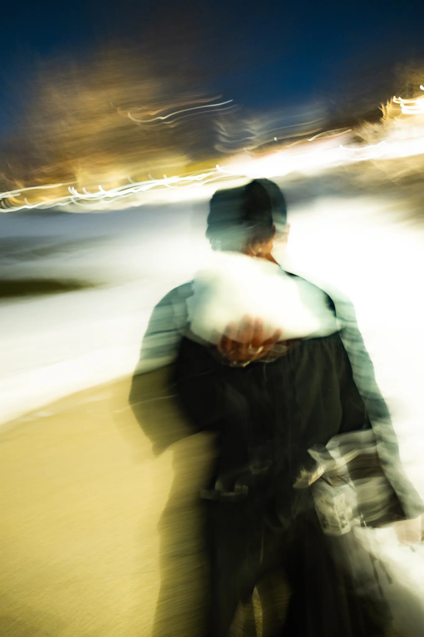 Motion-blurred figure in a cap walking a boardwalk at night, lights streaking past