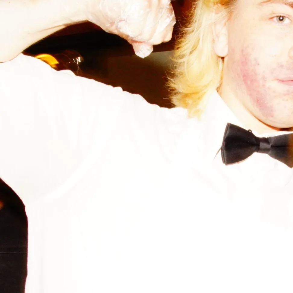Flash close-up of a blond partygoer in a bow tie raising an arm