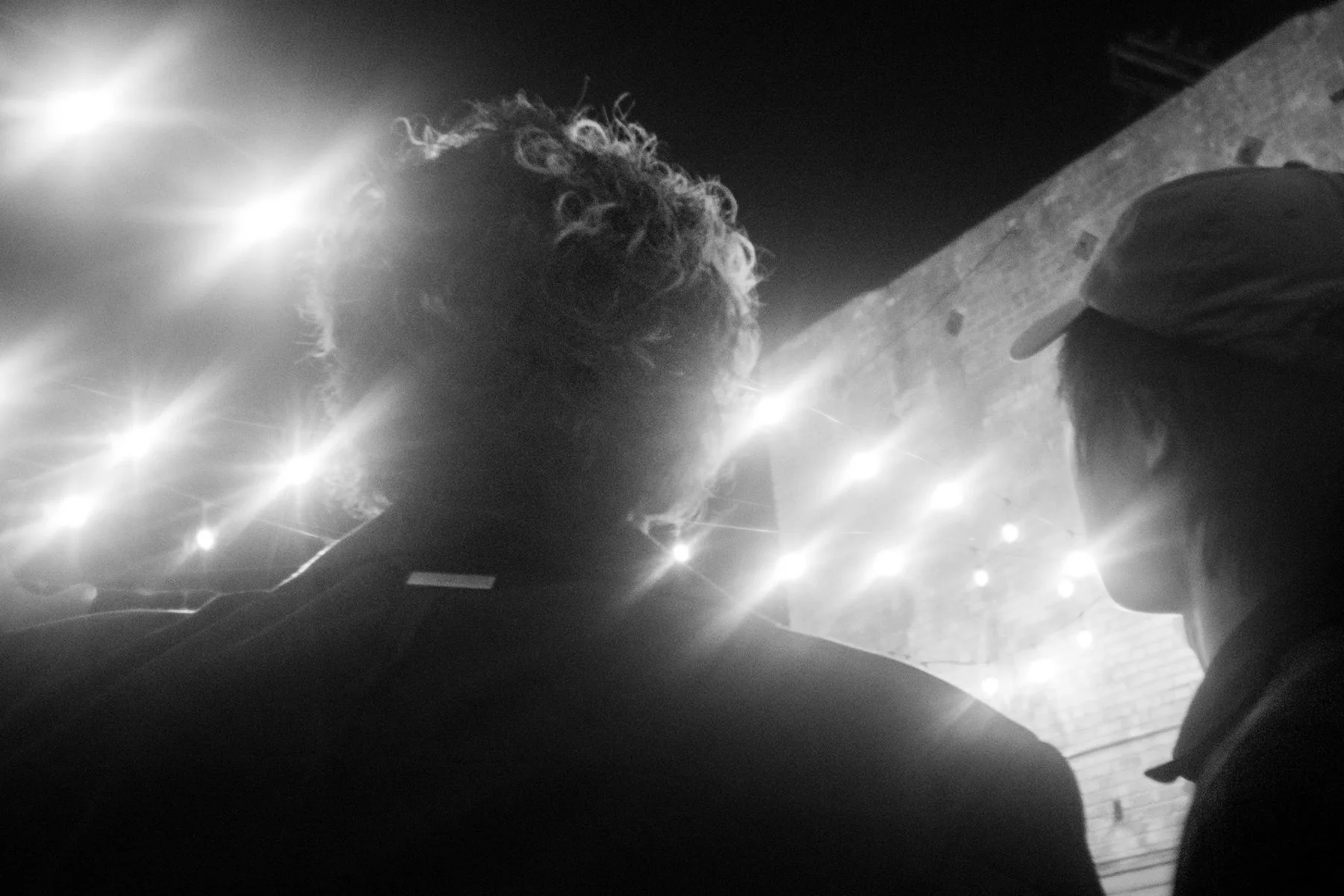 Black-and-white silhouettes of two heads against a wall of stage lights