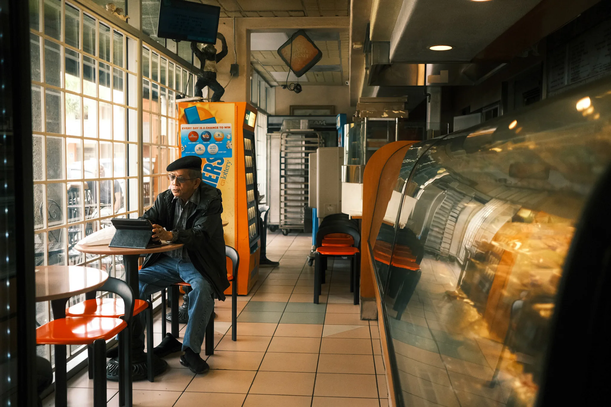 Man in a beret reading at a café table beside a barred window in an old diner