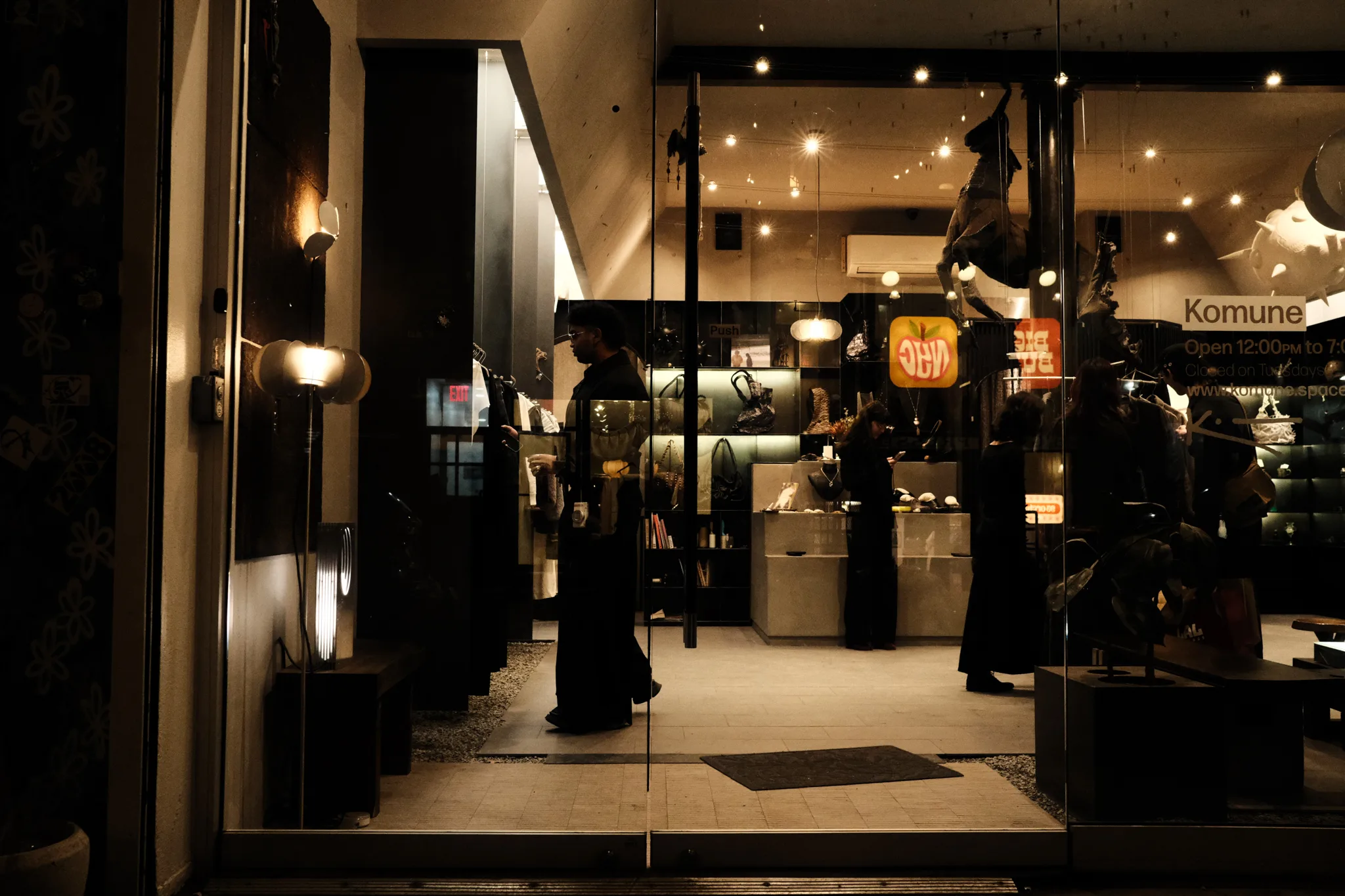 Night view into the warm-lit Komune boutique through its glass storefront