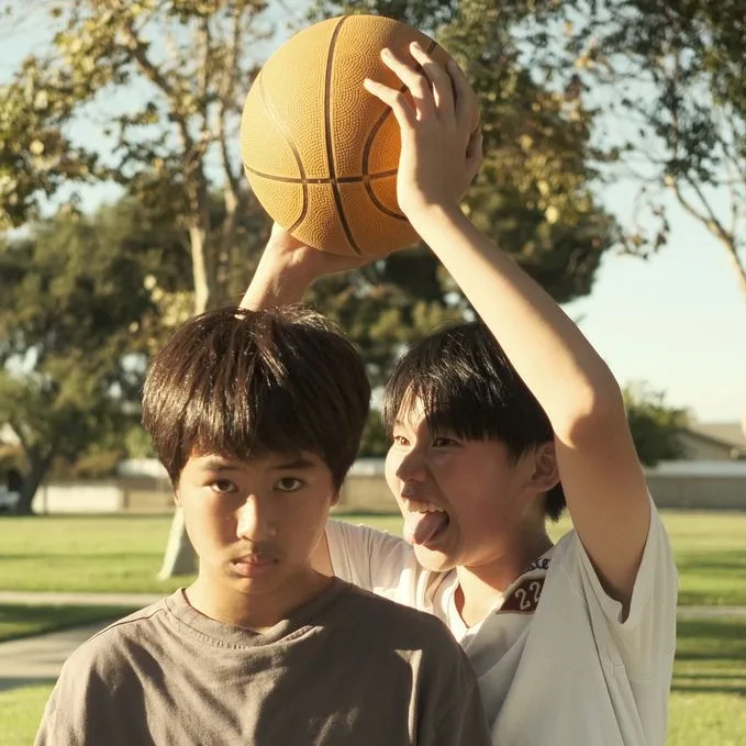 Two boys under a basketball held overhead in a sunlit park