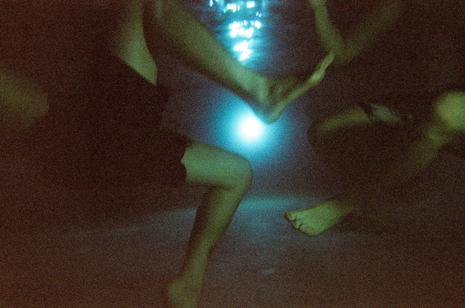 Legs and hands underwater around a glowing pool light, on film