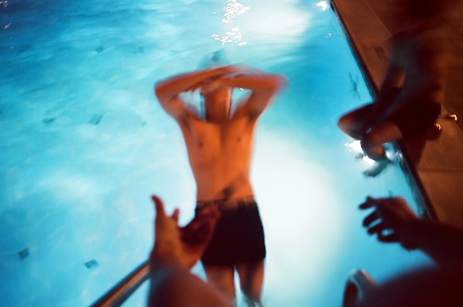 Blurred night swimmers climbing from a glowing blue pool
