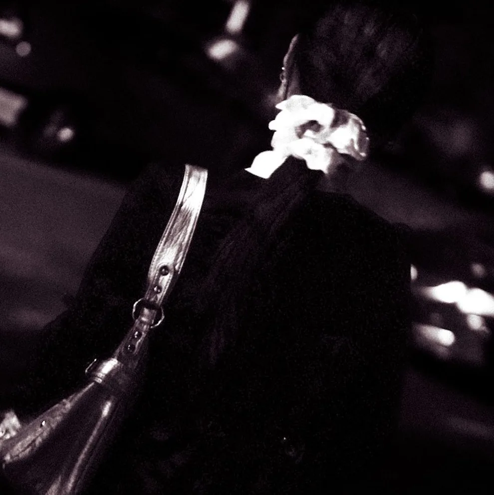 Black-and-white close frame of a white scrunchie and silver purse strap in a dark crowd