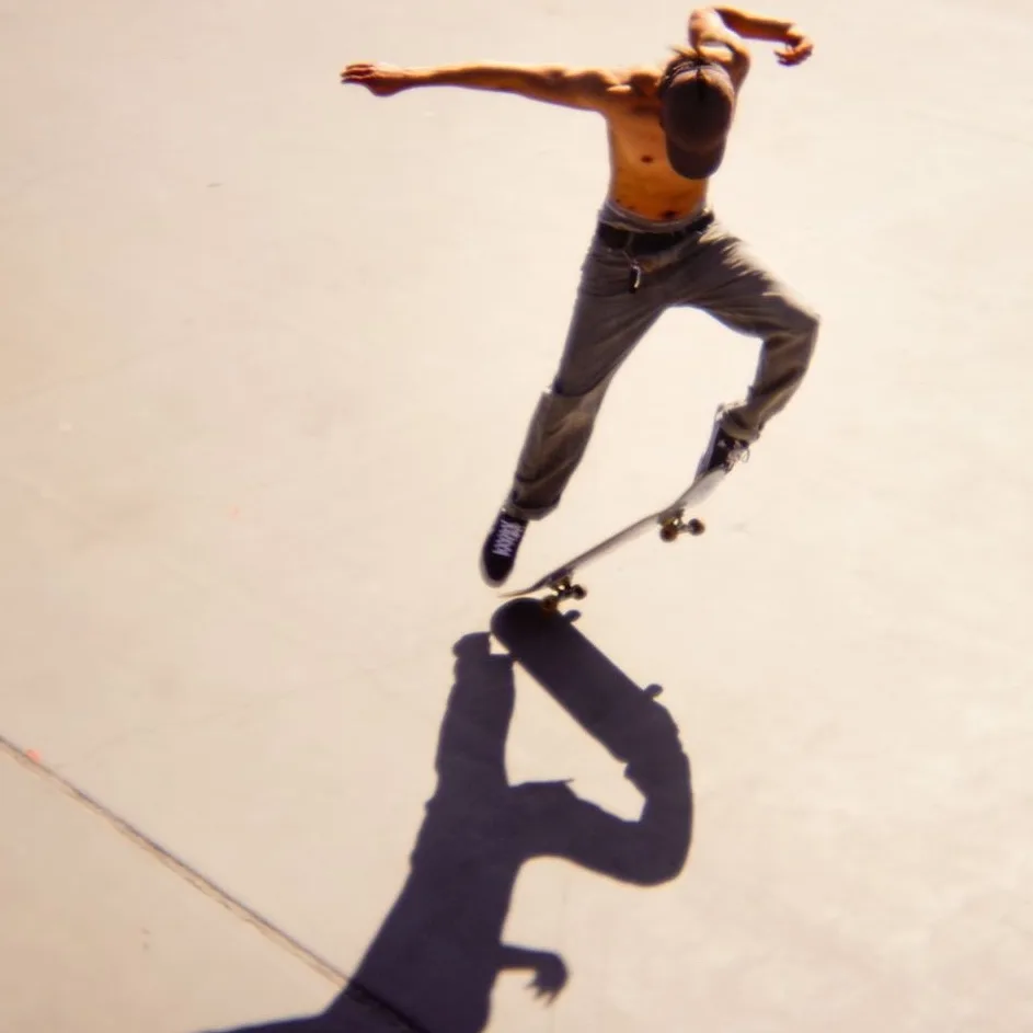 Skater mid-trick above his own shadow on sunlit concrete, shot from above