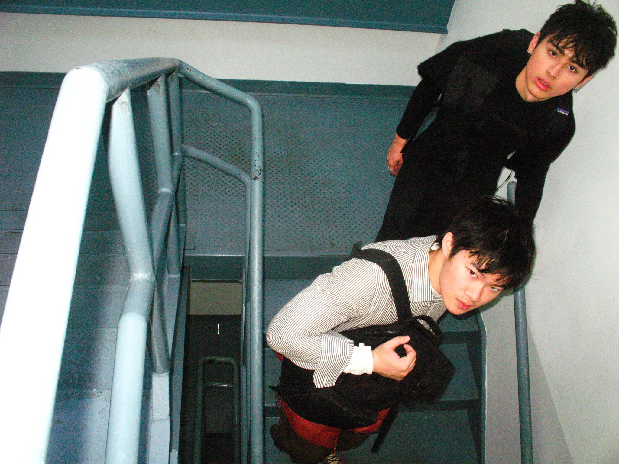 Two friends looking up a teal stairwell, shot with flash from above