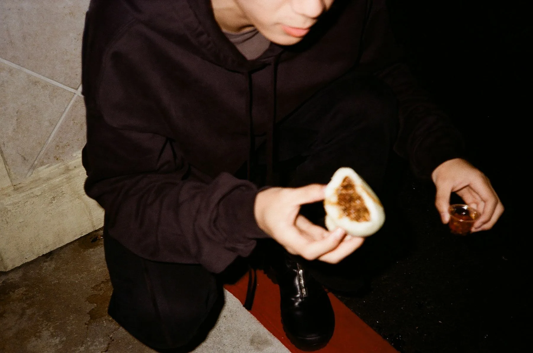 Hands holding a split steamed bun, crouched on a red-lit step