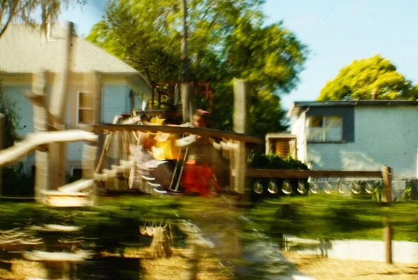 Motion-blurred yard with a swing set and playhouses seen from a passing car
