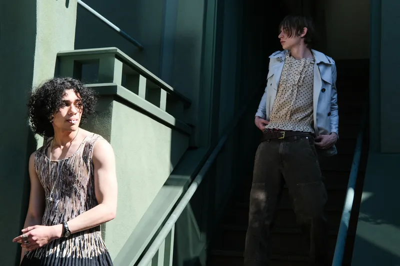 Two models in vintage outfits on a green apartment stairwell, one in a fringed tank, one in a polka-dot shirt and light trench