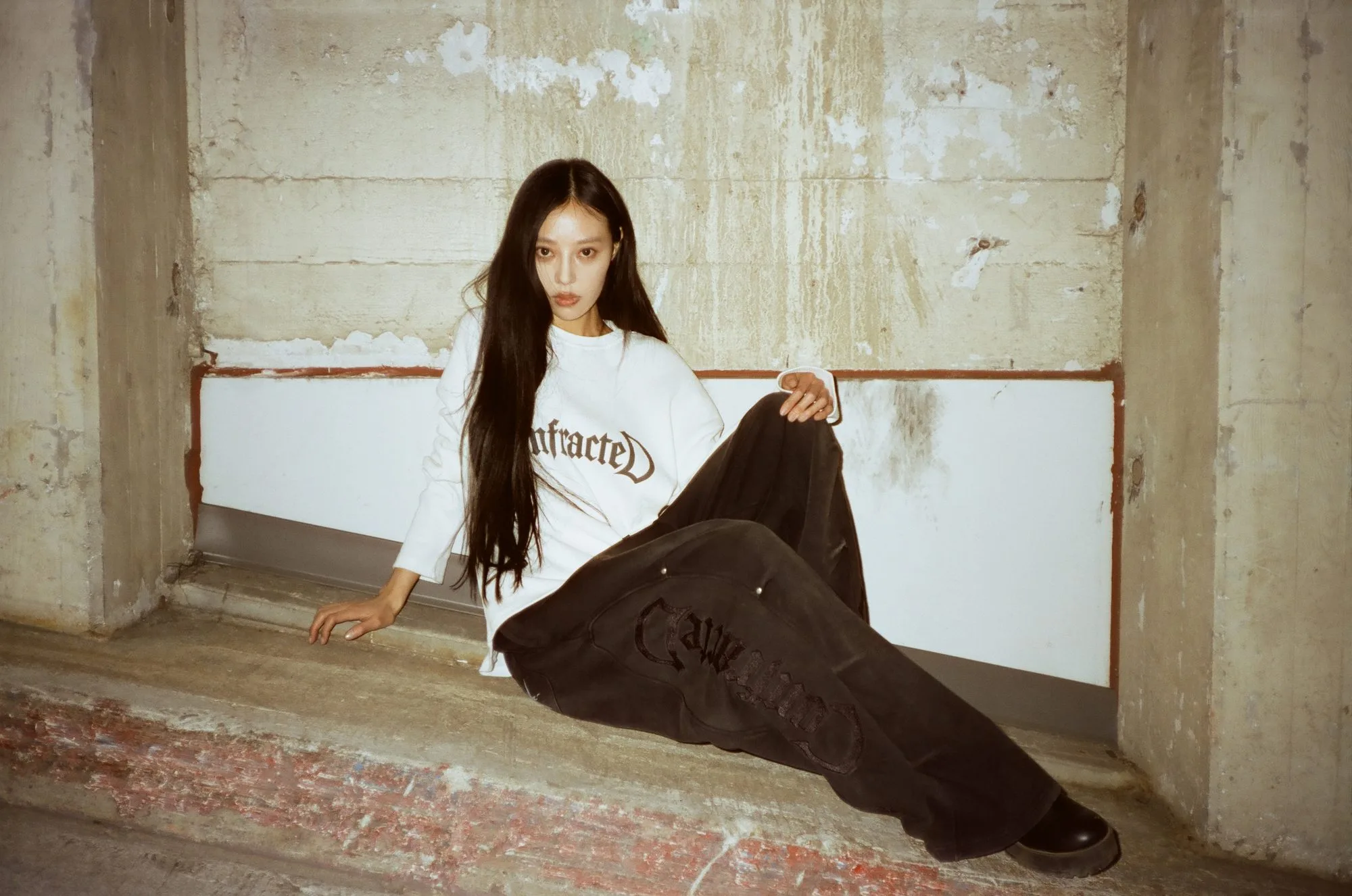 Model in a white Confracted long-sleeve seated in a raw concrete alcove, shot on flash film