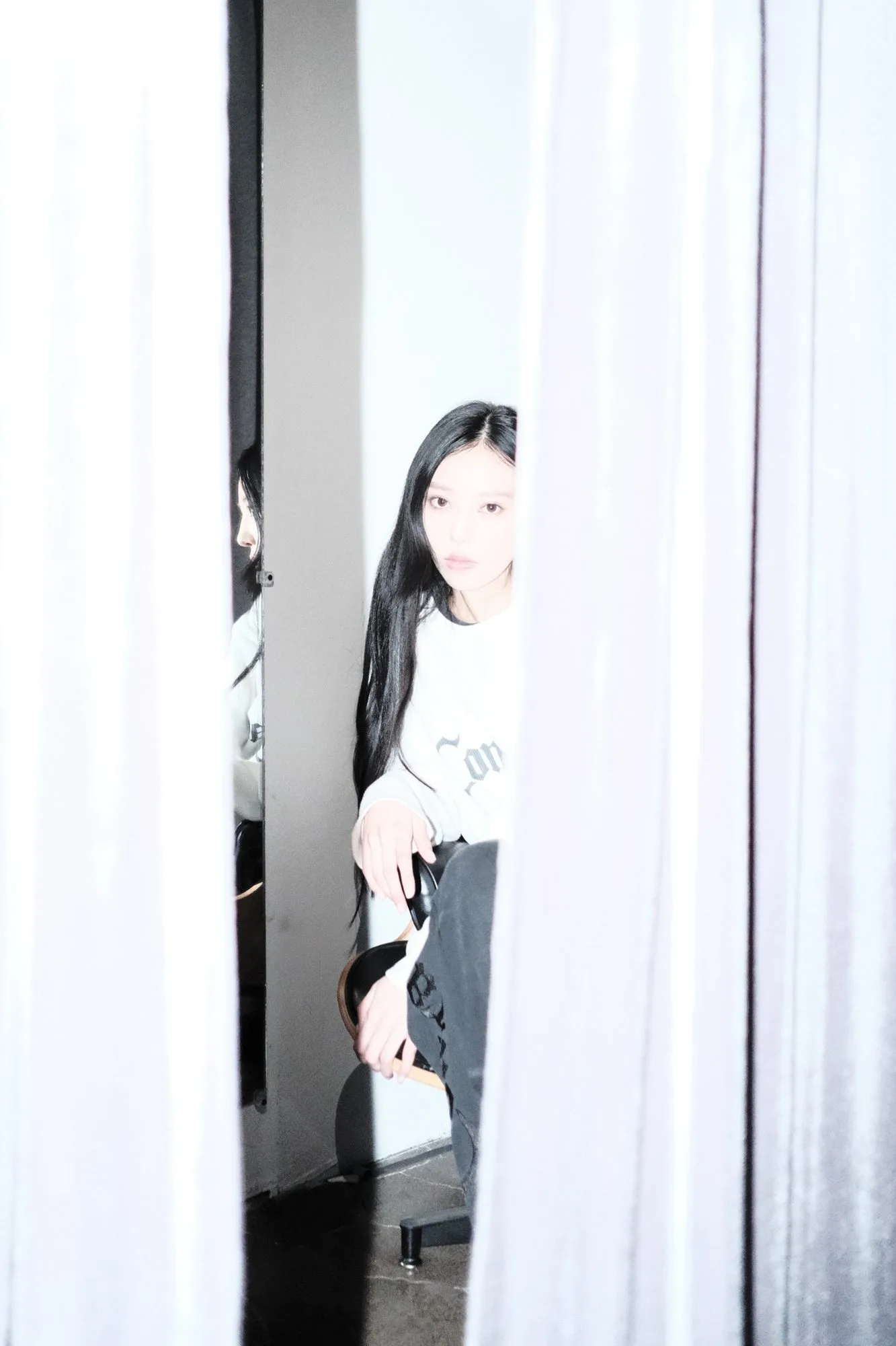 Flash portrait between white curtains of a model in a Confracted tee seated in a dressing room