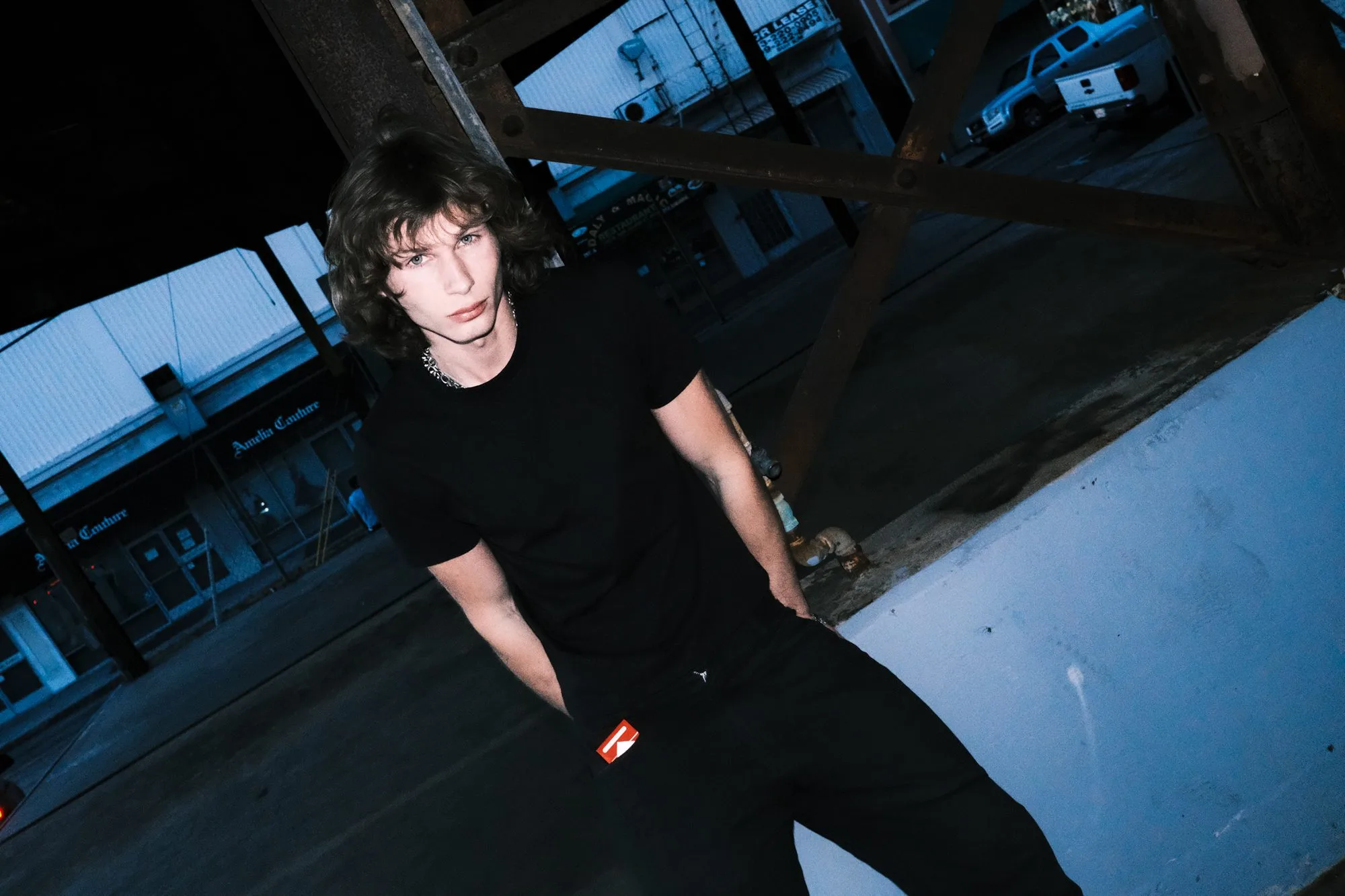 Flash-lit portrait of Dylan Wayne in black leaning against wooden beams at night