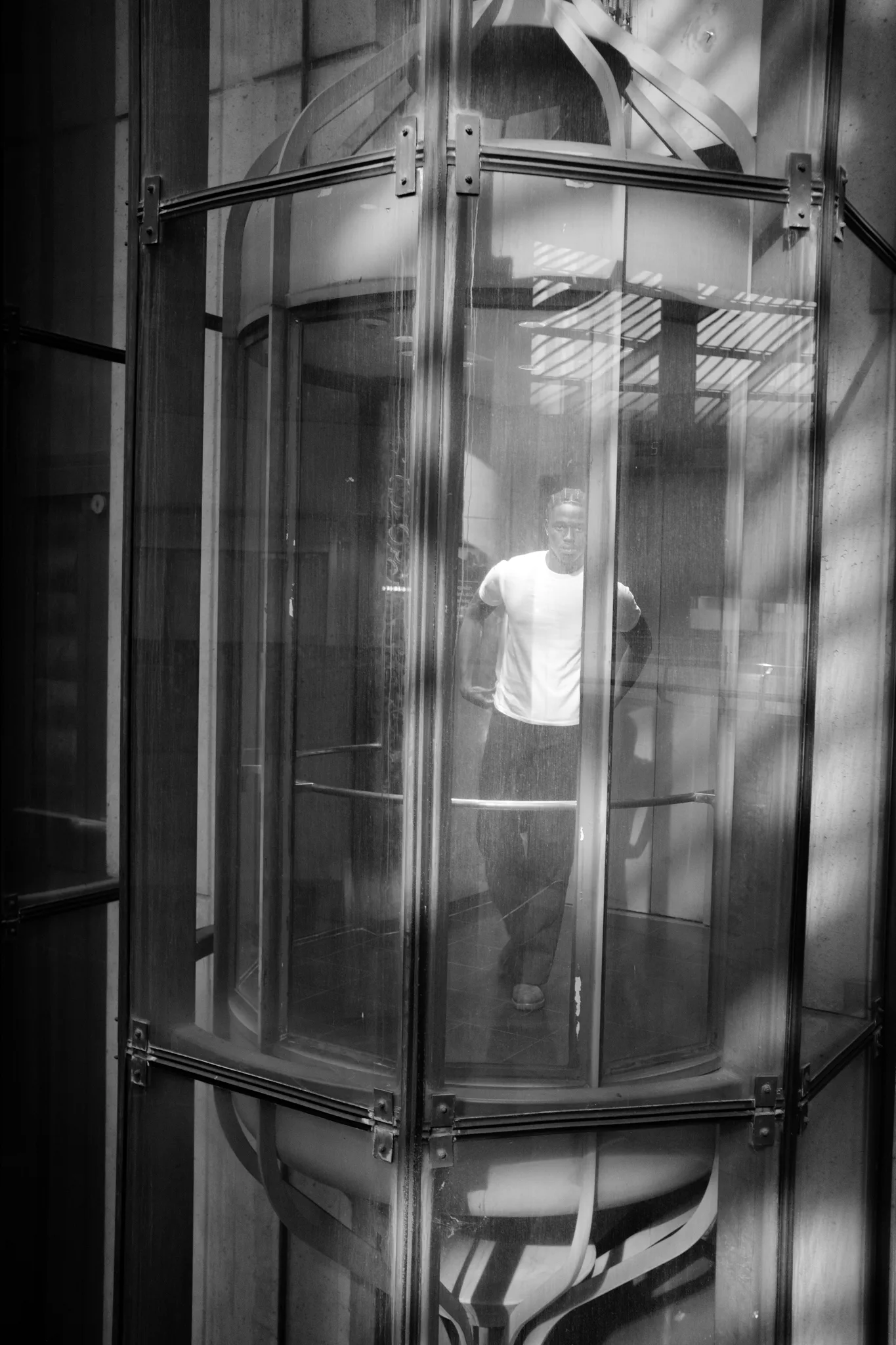 Black-and-white frame of a model seen through the curved glass of an elevator shaft