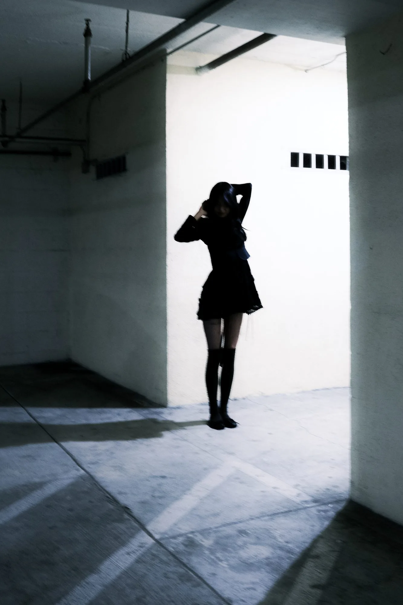 Model silhouetted in a bright doorway of an underground garage, wearing a dark skirt and knee-high socks
