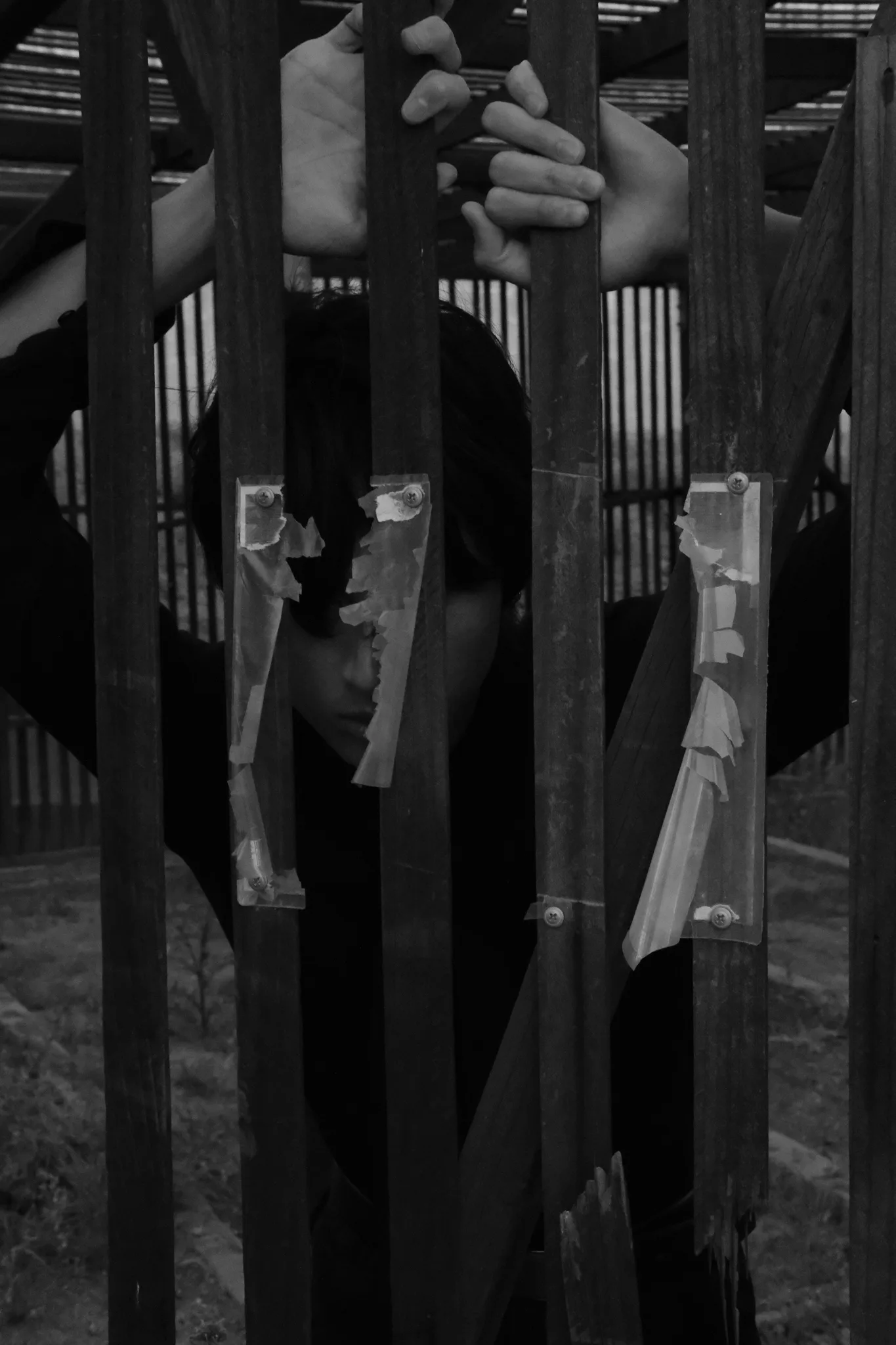 Black-and-white portrait of a model gripping weathered wooden slats, face half-hidden between them