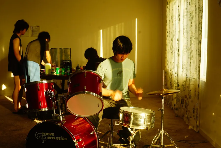 Drummer mid-beat at a red Groove Percussion kit in a warm sunlit practice room