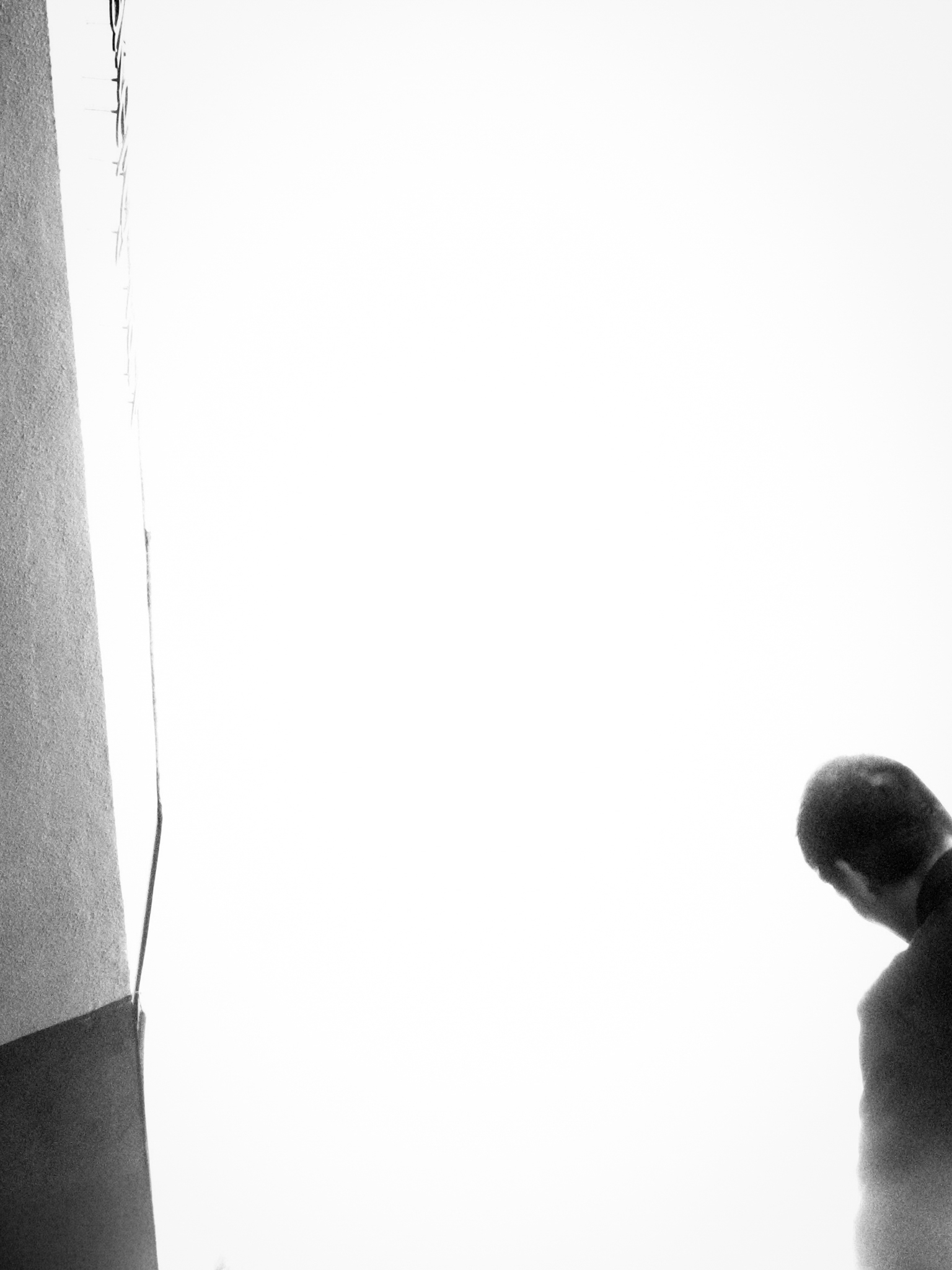 Minimal black-and-white frame of a figure's head entering the corner of a bright empty sky