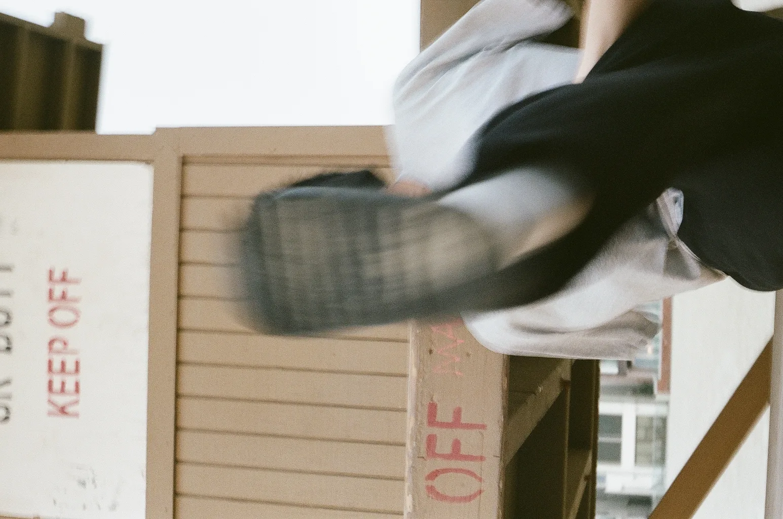 Blurred figure vaulting a wooden fence stamped 'KEEP OFF', the frame tilted sideways
