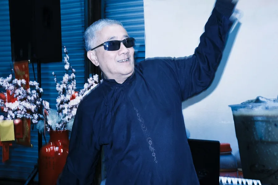 Man in dark sunglasses dancing beside red and white Lunar New Year flower arrangements