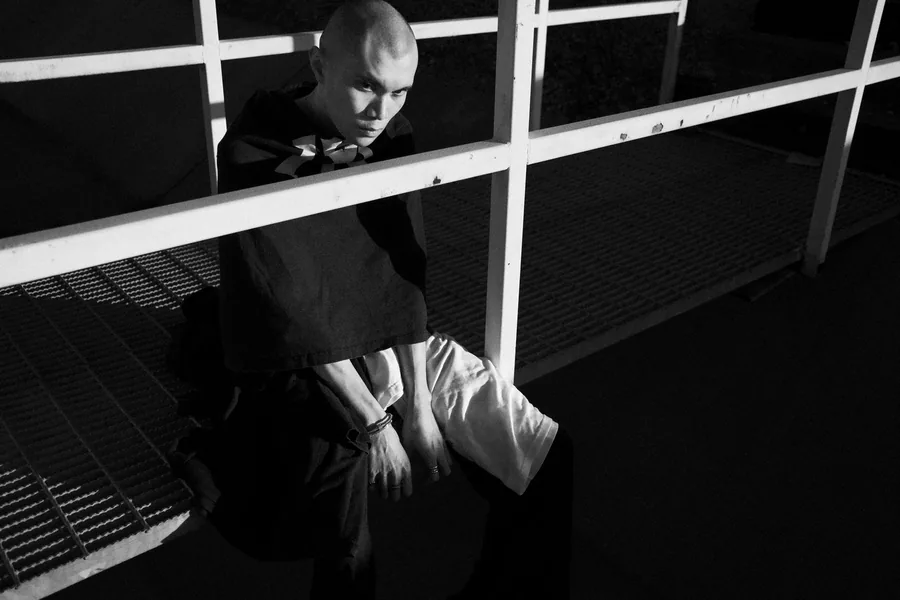 Black-and-white portrait of a man crouched beneath white metal railings at night