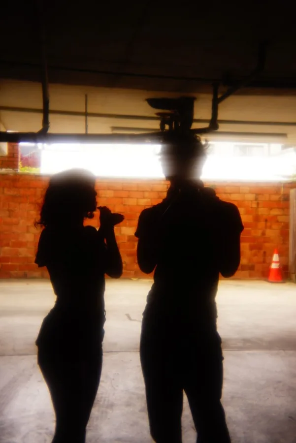 Two silhouetted figures in a parking garage, one raising a camera to film