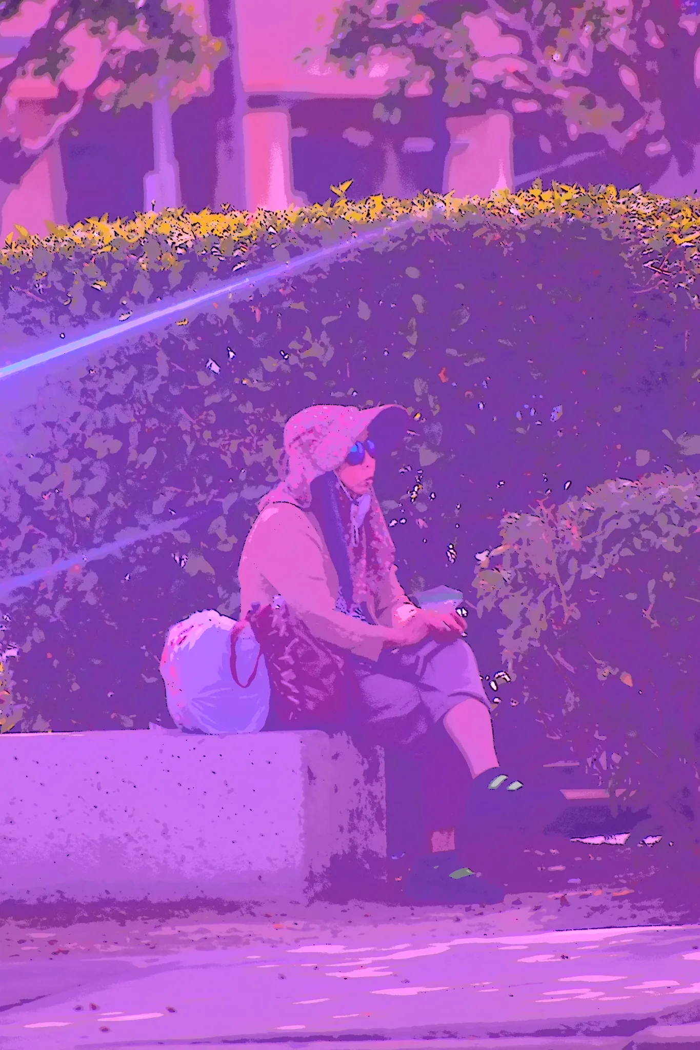 Heavily saturated purple-toned duotone photo of a woman in a sun hat and sunglasses sitting on a concrete bench beside a hedge with shopping bags