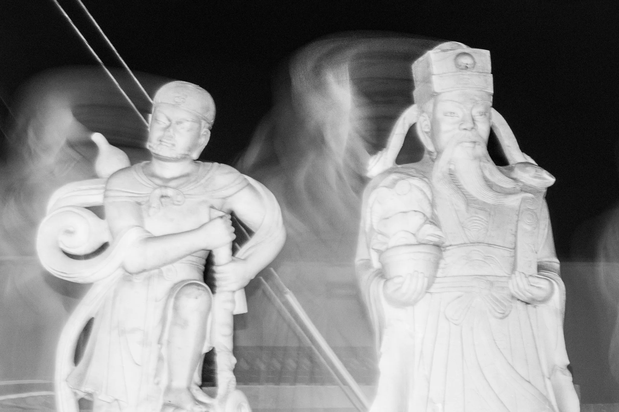 Black-and-white long exposure of two temple guardian statues with ghosted motion trails