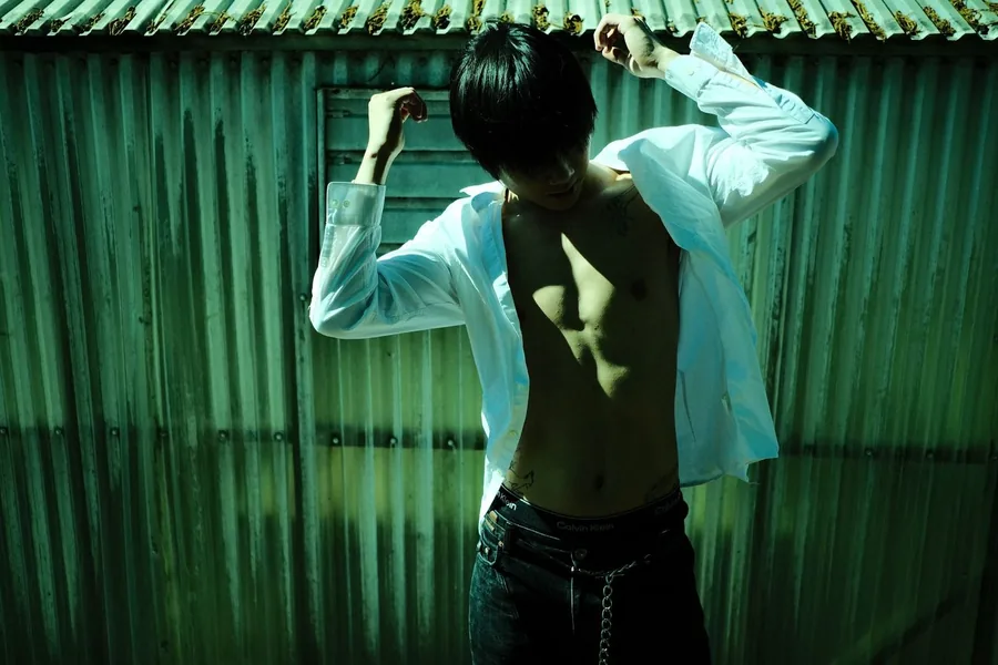 Model in an open white shirt posed against a green corrugated metal wall