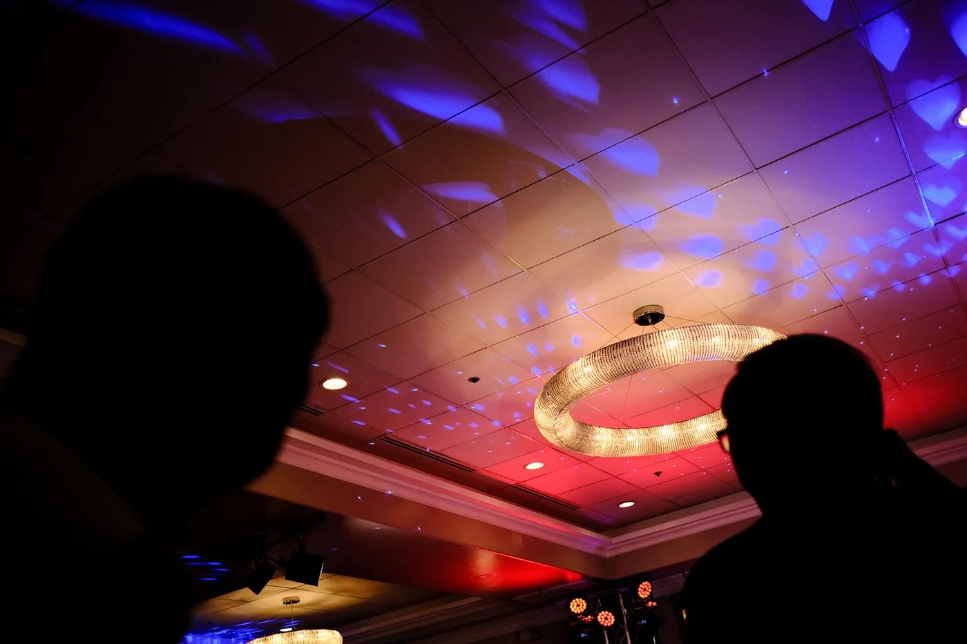 Banquet-hall ceiling washed in red and blue party light around a crystal chandelier