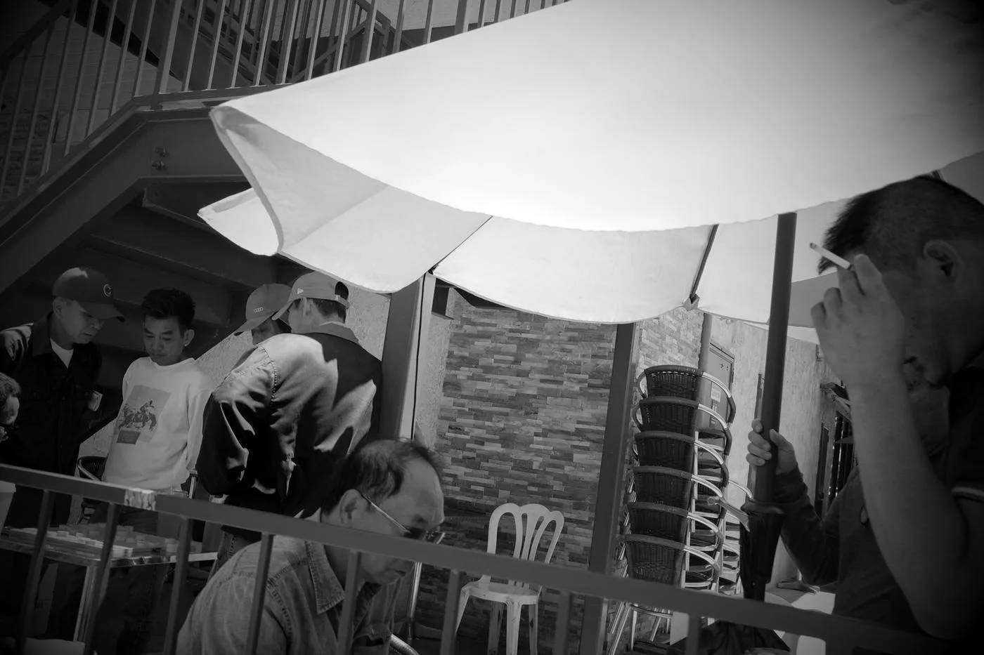 Black-and-white scene under a café umbrella of older men gathered at outdoor tables