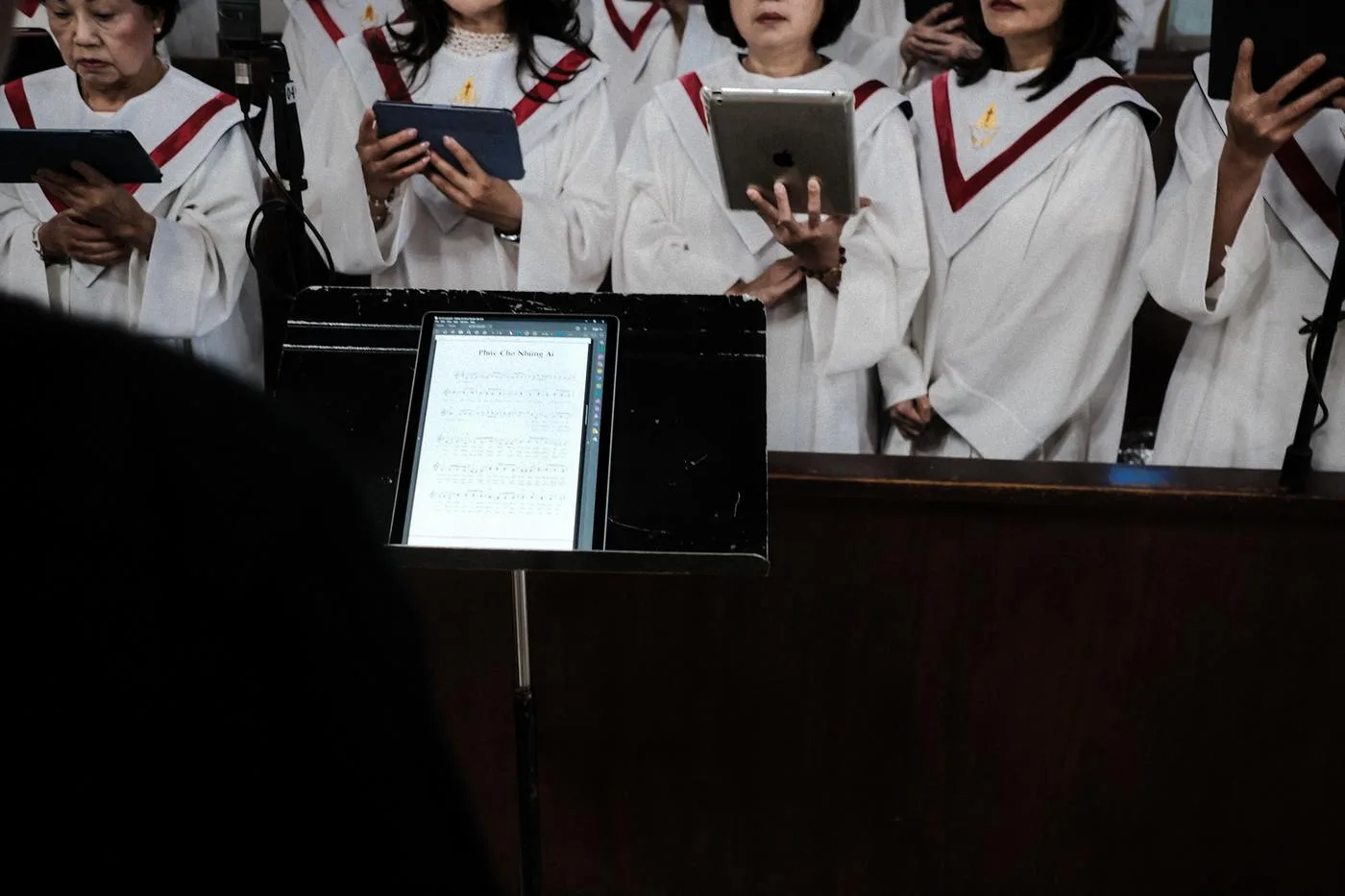 Choir in white robes singing from tablets, a sheet-music stand in the foreground