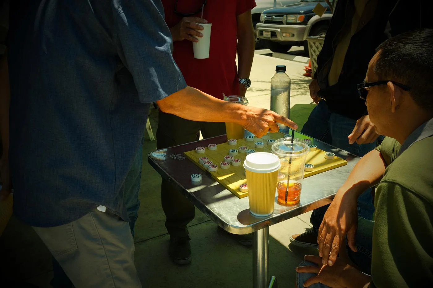 Hands moving pieces in a street game of cờ tướng beside iced drinks