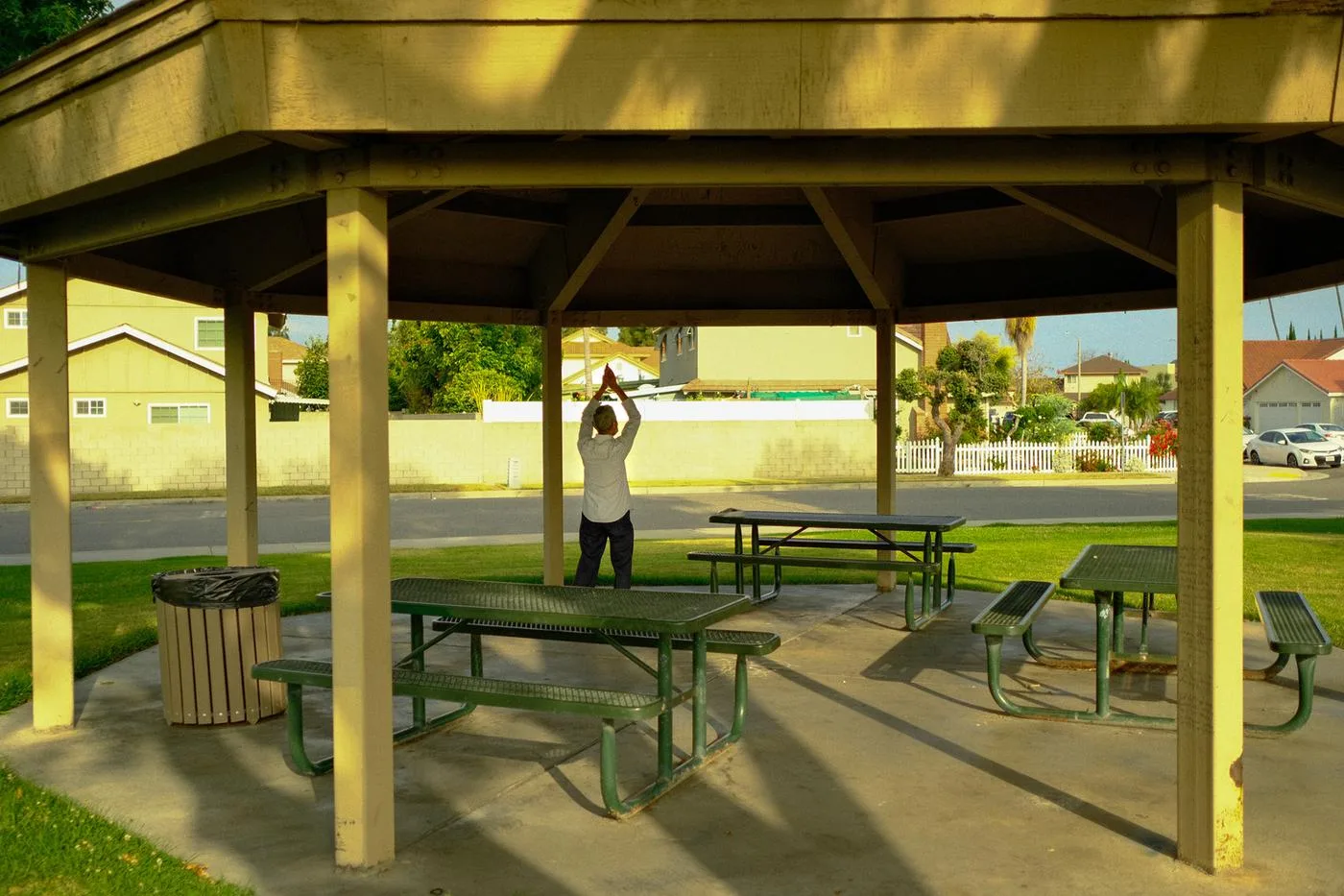 Person stretching under a park gazebo between green picnic tables