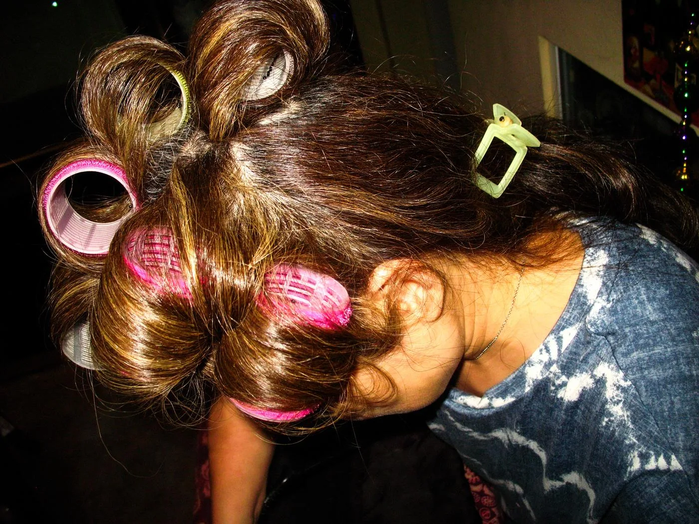 Girl's hair set in pink rollers, head bowed in warm lamplight