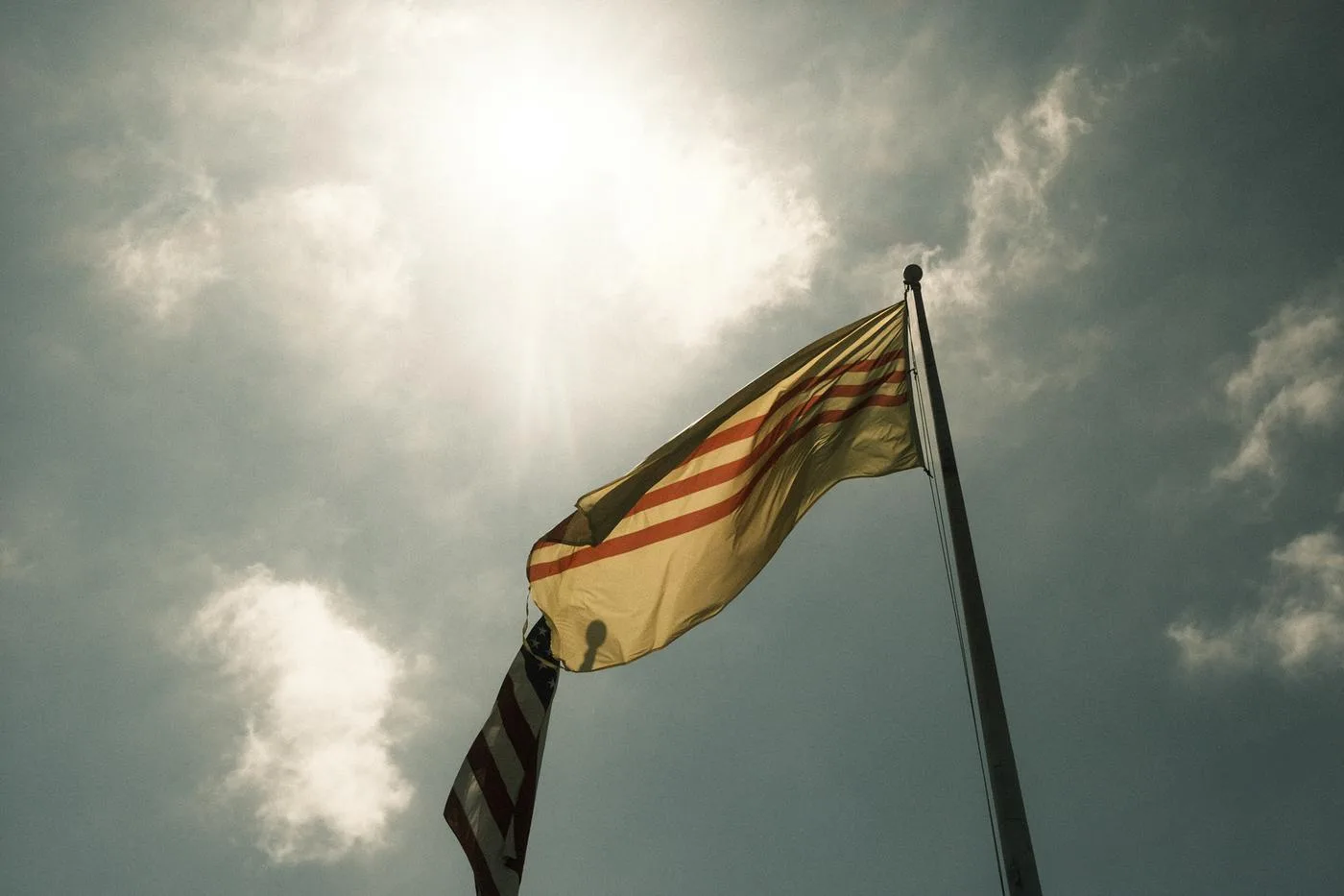 South Vietnamese heritage flag and US flag backlit against a clouded sun
