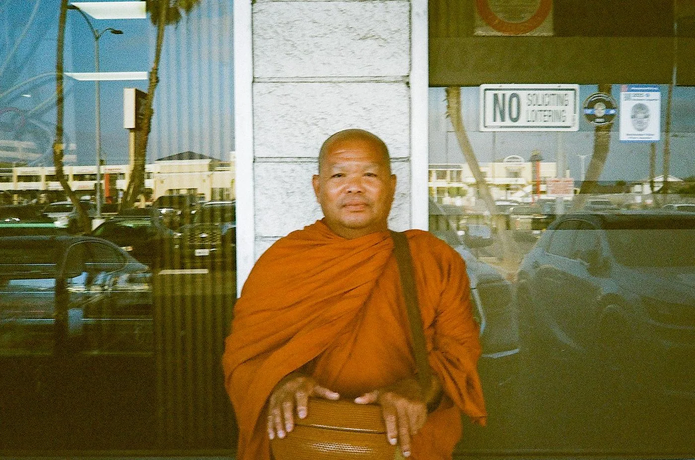 Monk in orange robes with a satchel standing before a reflective storefront