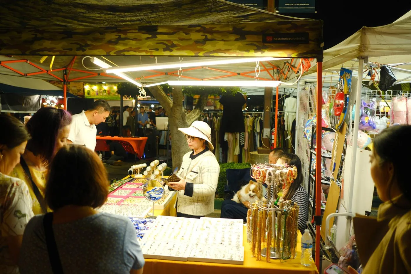 Vendor in a white hat selling jewelry under a night-market tent