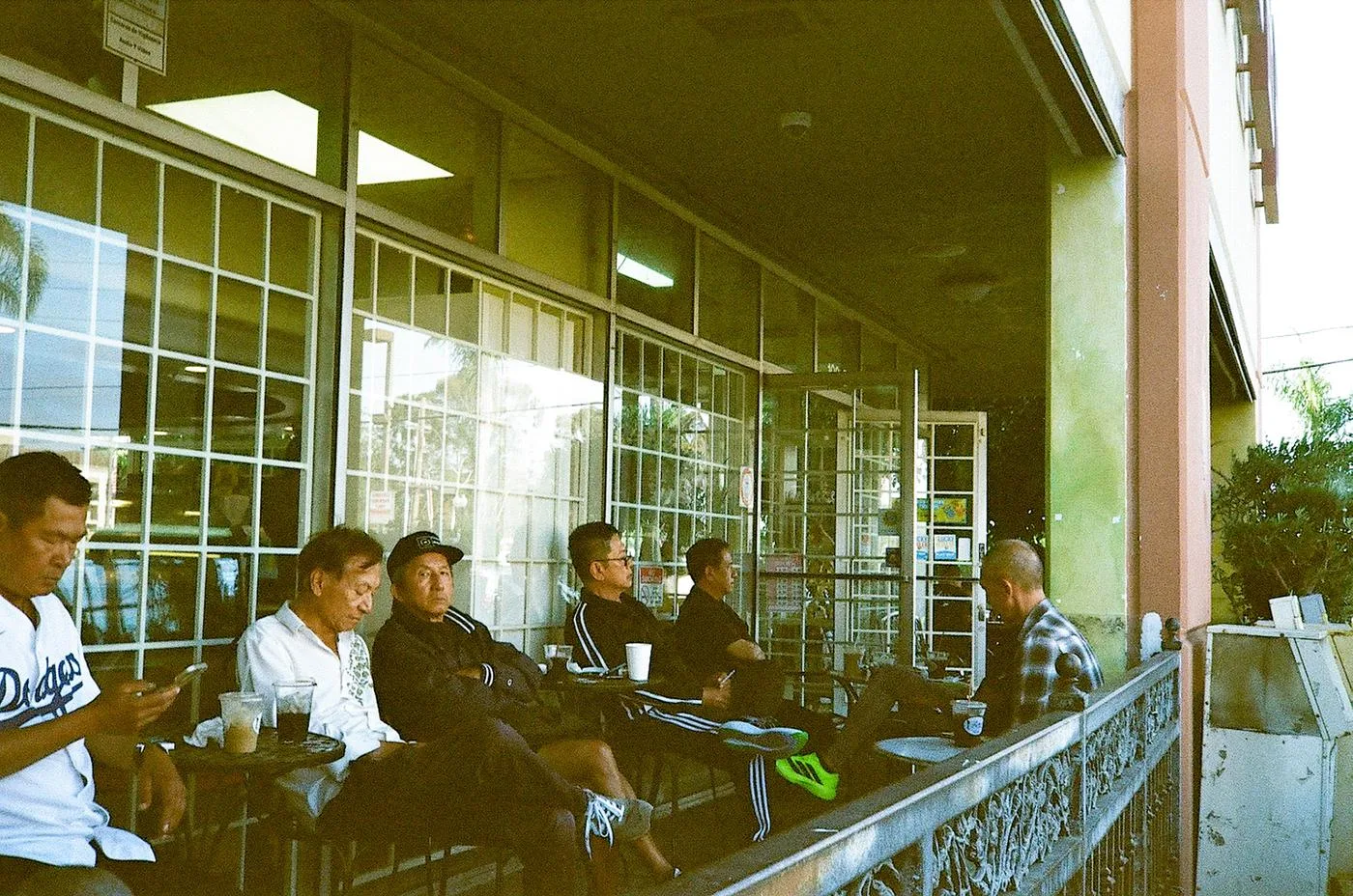 Men gathered with coffees along a plaza rail in late-afternoon light