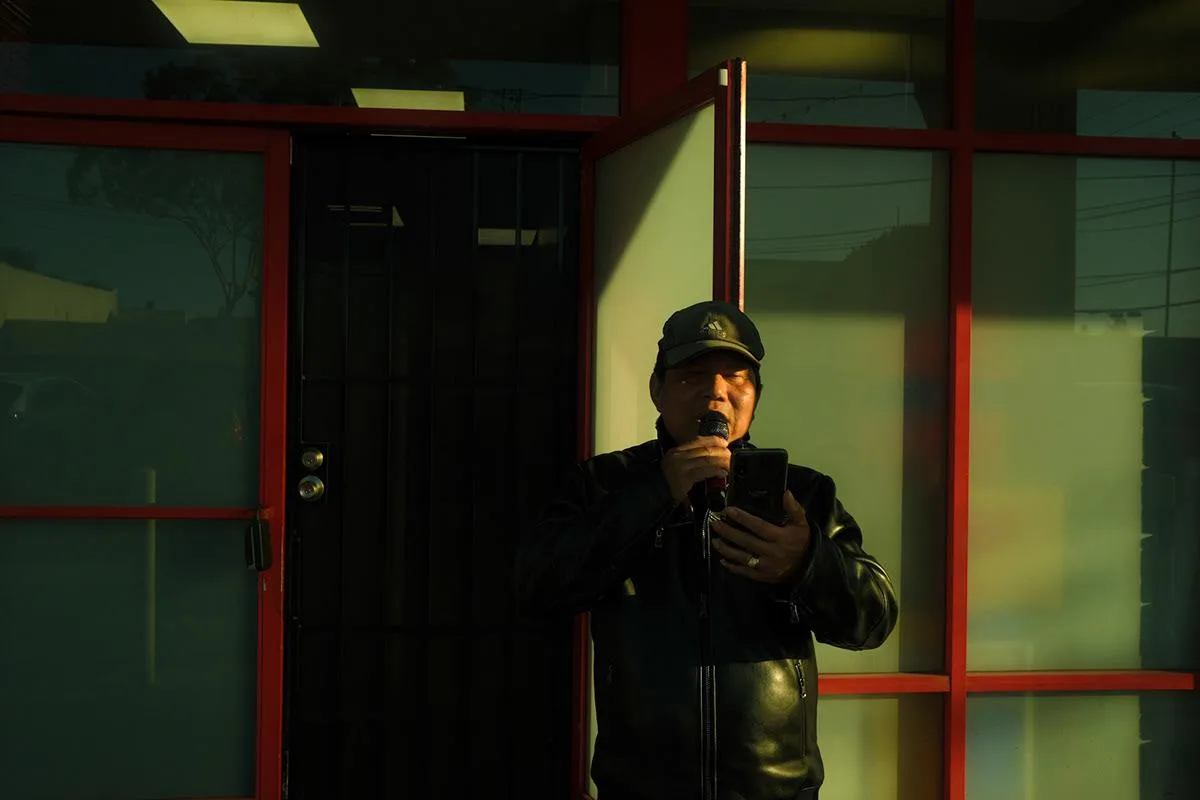 Man in a cap and leather jacket on his phone beside red-framed windows in low sun
