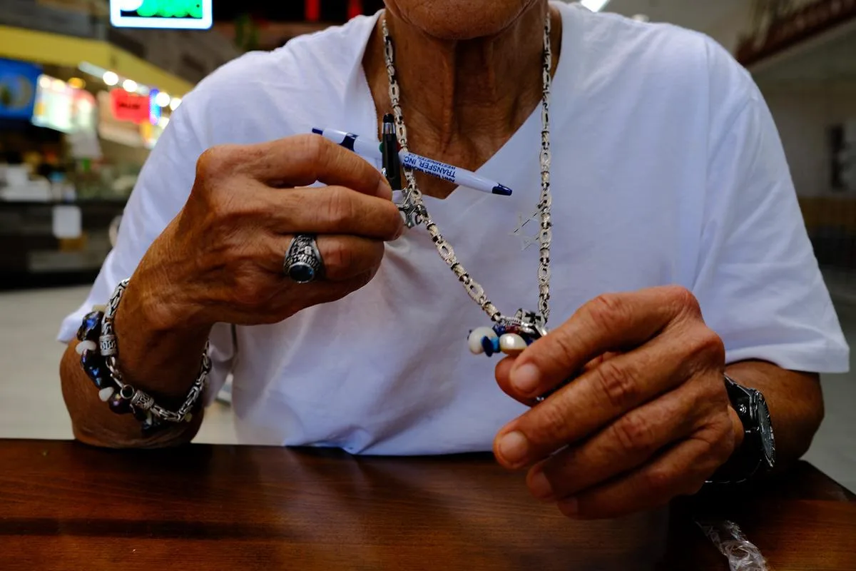 Close-up of weathered hands threading a beaded necklace at a wooden table