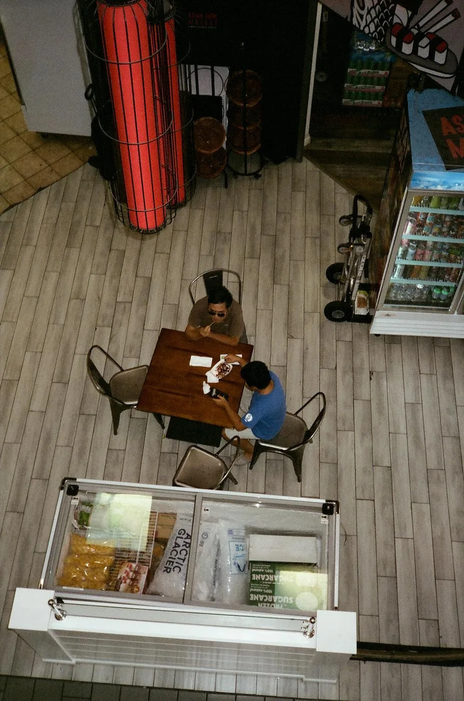 High view of two men at a café table beside a freezer of sugarcane and juice