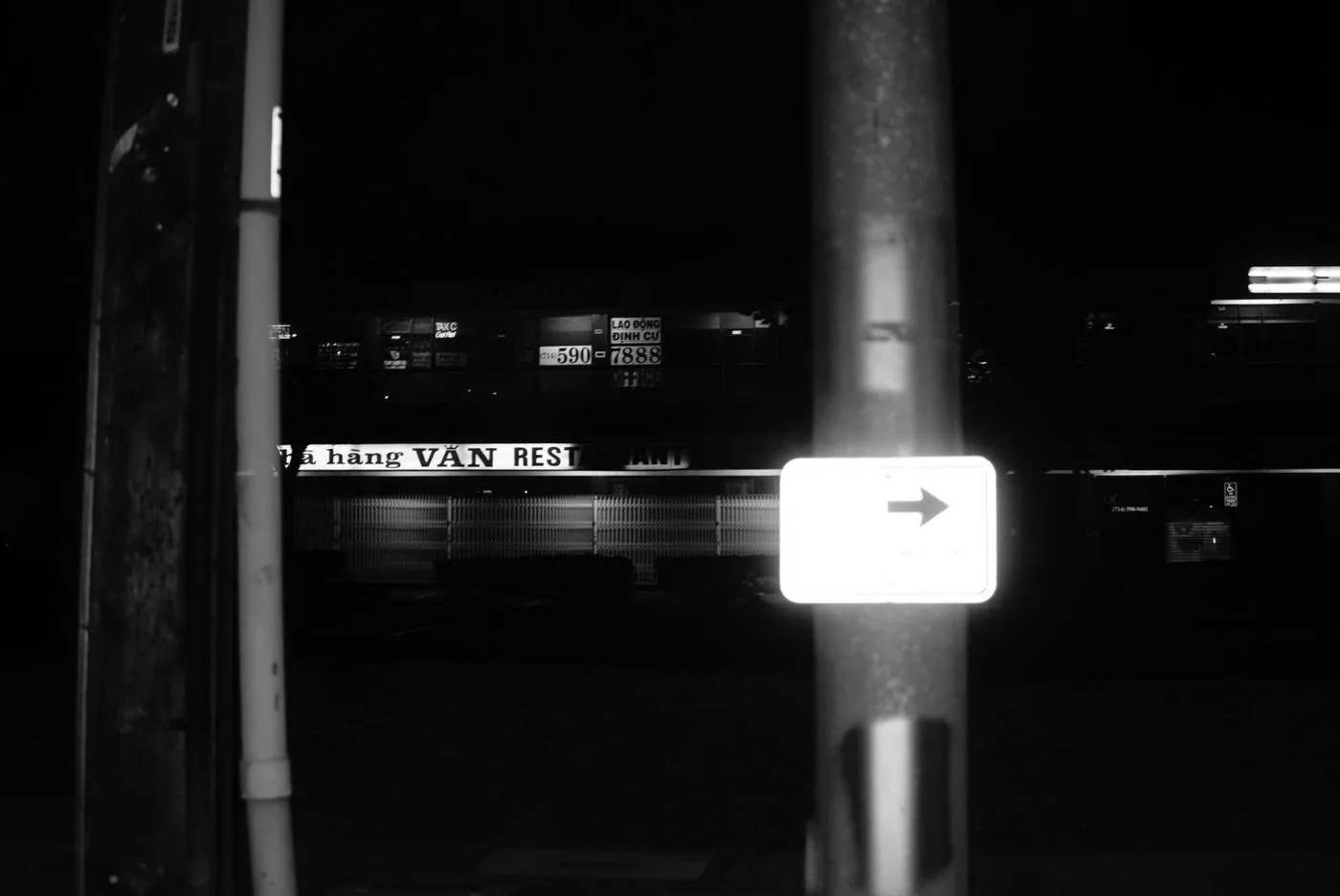 Black-and-white night frame of a lit arrow sign and Vietnamese restaurant signage