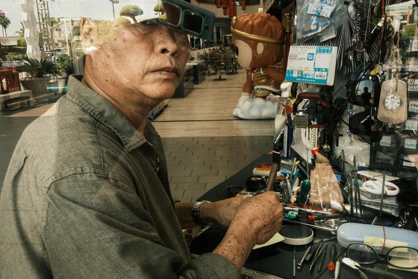 Watch repairman at his bench surrounded by tools, seen through the shop window