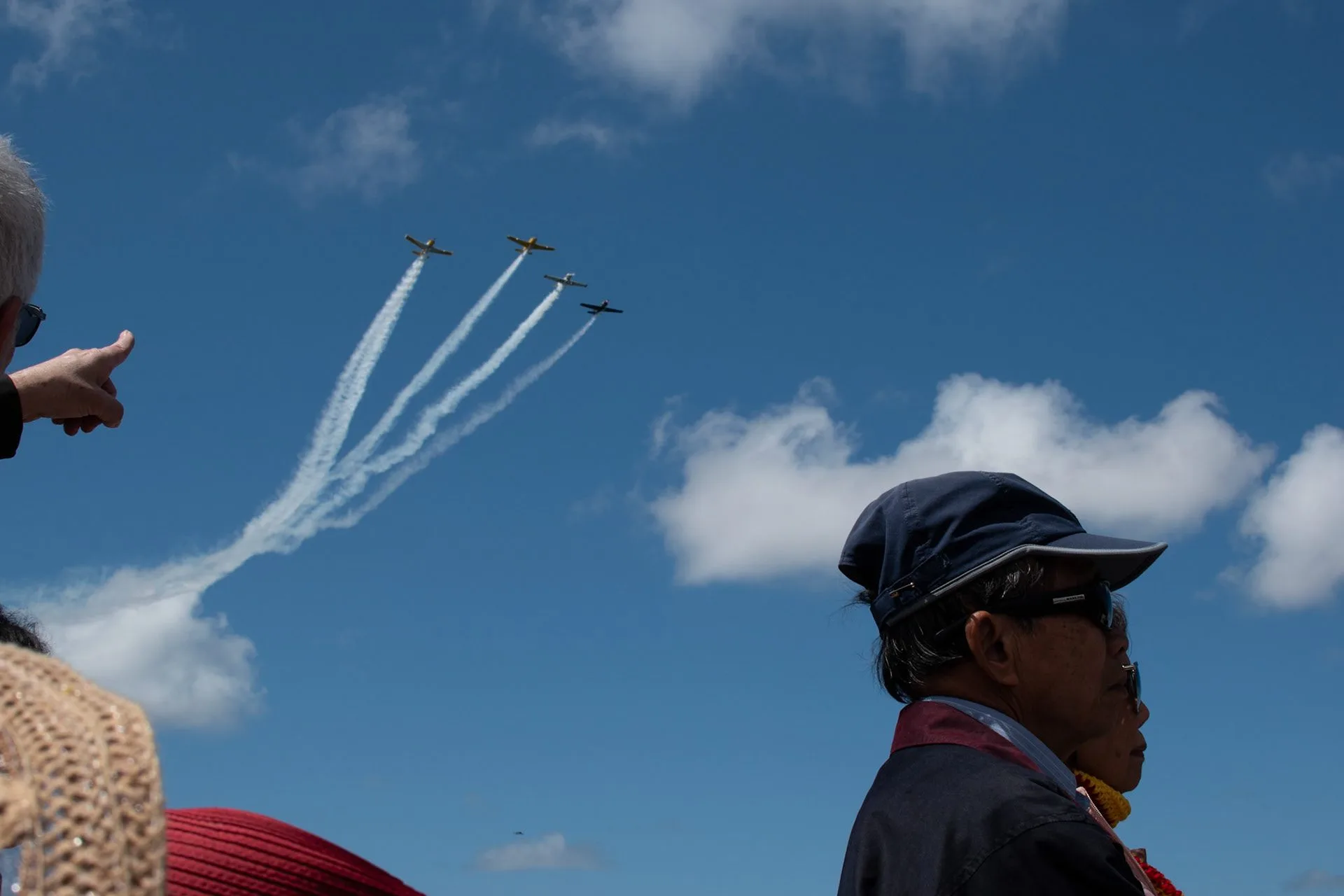 Onlooker pointing at four jets trailing smoke in formation across a blue sky